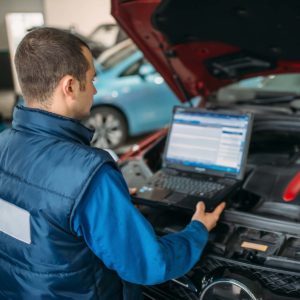 Engineer with laptop makes computer diagnostics of the car engine in auto-service. Vehicle wiring inspection